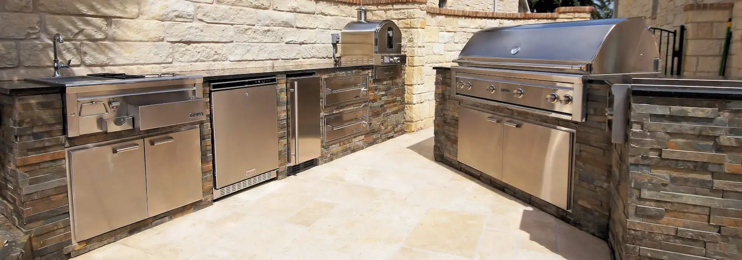 A stone wall and an outdoor kitchen with stainless steel appliances.